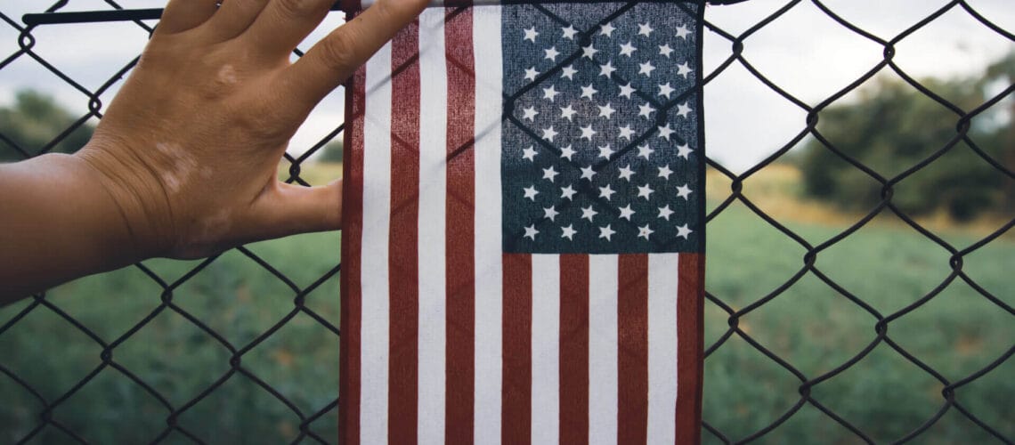Persona sosteniendo la bandera de EE.UU. contra una reja, conceptualizando los controversiales cambios en el proceso de asilo en Estados Unidos