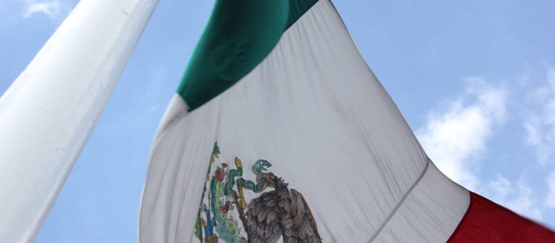 Imagen de cerca de la bandera de México flameante de un poste representando la crisis fronteriza que azota la nación