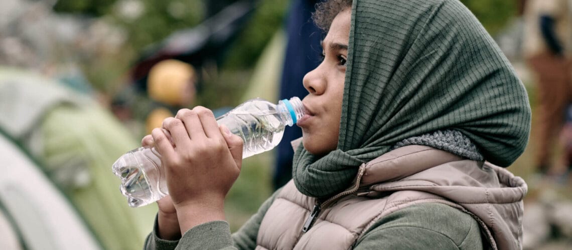 Joven migrante tomando agua en un campamento de refugiados tras aprender como pedir refugio en estados unidos con su familia