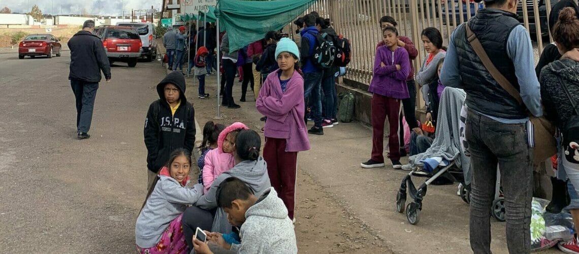 Este artículo habla sobre el Estatus de Protección Temporal para América Central. La imagen muestra a un grupo de migrantes esperando en la frontera sur de los EEUU.