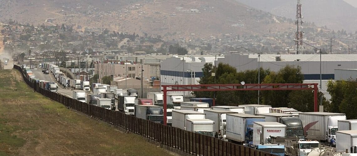 Este artículo habla sobre el bloqueo en la frontera. La imagen muestra una fila de camiones esperando para ingresar a los Estados Unidos por vía terrestre.